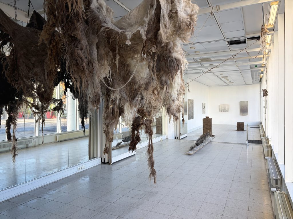 Näkymä Art Space Marin etuovelta näyttelytilaan. Kuvan etualalla katosta roikkuva lampaanvillasta tehty installaatio.